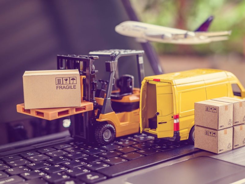 Logistics, supply chain and delivery service concept : Fork-lift truck moves a pallet with box carton. Van on a laptop computer, depicts wide spread of products around globe in ecommerce popular era